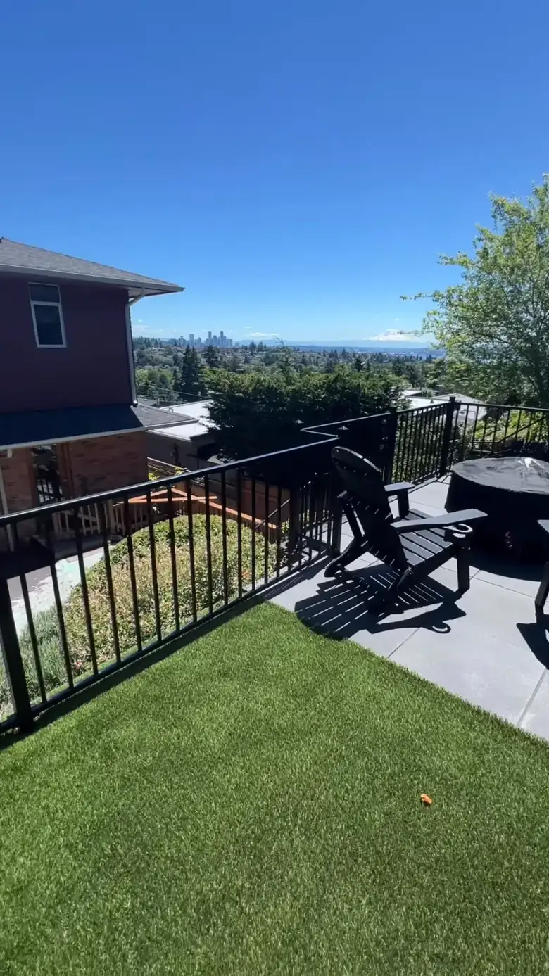 Looking out from a Magnolia terrace over a black metal rail to the downtown Seattle skyline, with artificial turf, a fire table and black Adirondack chairs in the foreground