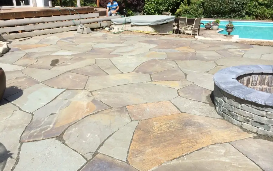 Irregular flagstone terrace fitted around a hot tub and a circular fire pit in a Wedgwood garden