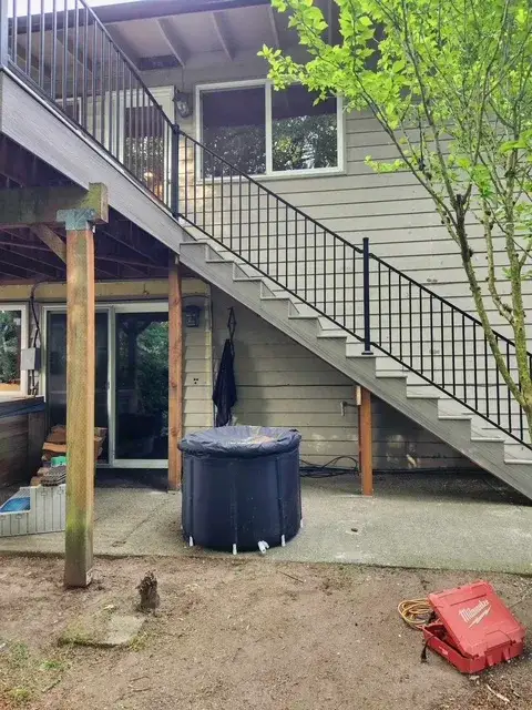 Newly built exterior stairs with black metal railing running down the side of a West Seattle house from the deck above to the lower patio