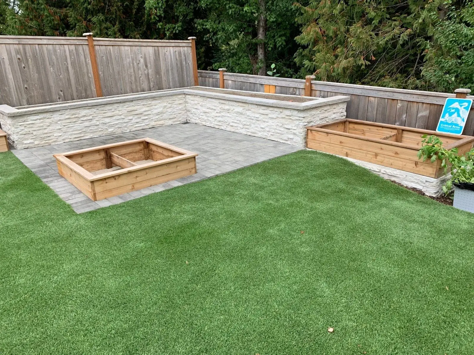 Artificial turf lawn framed by cedar raised planter beds and a paved seating area