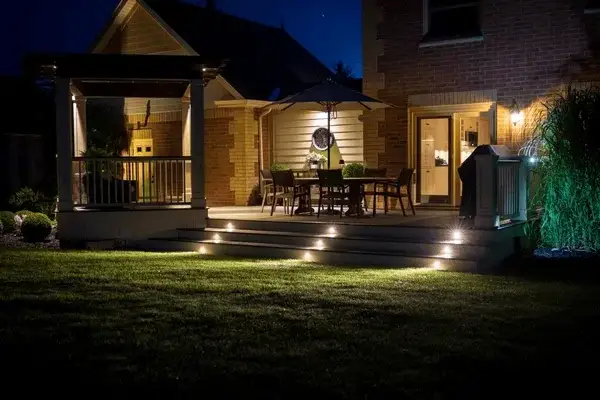 Covered brick patio lit at night with recessed step lights and warm downlights over dining furniture