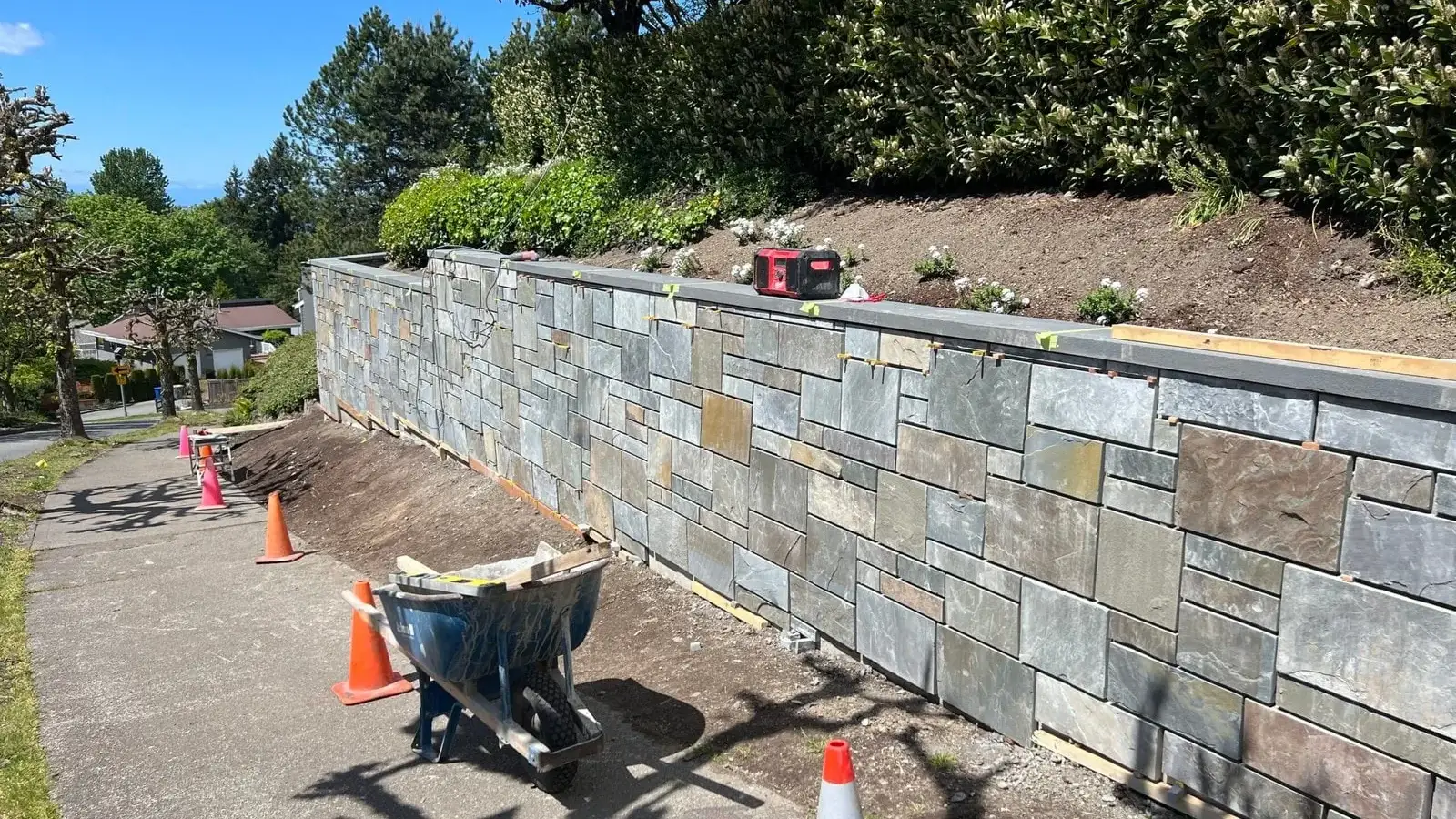 Natural stone veneer retaining wall under construction with tools and materials on site