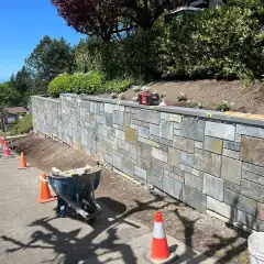 Natural stone veneer retaining wall under construction with tools and materials on site