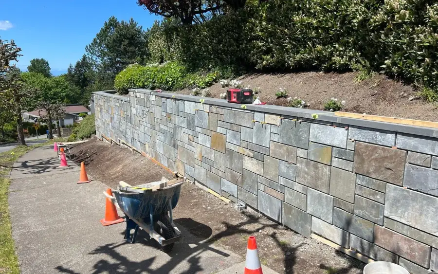 Natural stone veneer retaining wall under construction with tools and materials on a Woodinville site