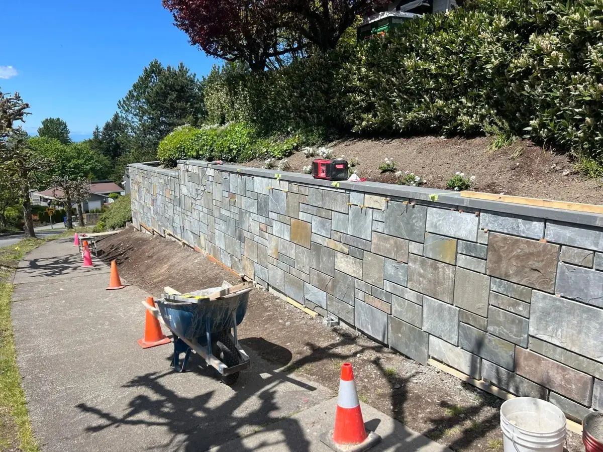 Natural stone veneer retaining wall under construction with tools and materials on site
